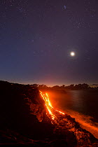 Hot  lava from the 61G flow, emanating from Pu'u O'o on Kilauea Volcano, flows over sea cliffs into the ocean under the stars and moon, Kamokuna, Kalapana, Hawaii Volcanoes National Park, Puna, Hawaii...