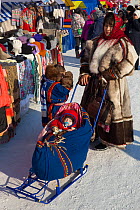Nenets woman pushing her baby in a cradle on skiis at the reindeer herders' festival in Nadym. Yamal, Western Siberia, Russia.