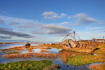 Old boats alongside channel with rising tide in Dee Estuary in early morning sunlight. Heswall, Wirral, Merseyside, UK January.