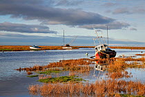 Old boats alongside channel with rising tide,  Dee Estuary,  early morning sunlight near Heswall, Wirral, Merseyside, UK January.