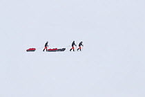 Three people skiing across snow pulling sledges, winter, Spitsbergen, Svalbard, Norway, April. 2016.