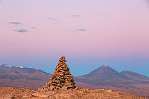 Apacheta / Apachita - a stone cairn in the Andes, a little pile of rocks built along the trail in the high mountains with Licancabur volcano (5916 m above sea level) and Juriques volcano to the far ri...