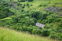Railway cottages, Chee Dale, Peak District National Park, Derbyshire, UK. Quarried limestone rockfaces can be seen along the ridge above.