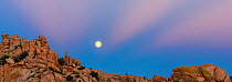 Full moon rising over Texas Canyon's granite boulders in evening light with last rays of sunset. Arizona, USA. August.