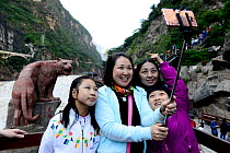 Chinese tourists taking  selfie photos in front of statue in Tiger Leaping Gorge, Haba Xue Shan Range. Yunnan, China, October 2016..