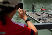 Person taking photograph of Smooth coated otter (Lutrogale perspicillate) resting on a dock, Singapore. November.
