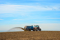 Tractor pulling tank spreading slurry over arable field, Dover, Kent, UK. July