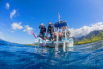 Divers step off a dive boat into the Pacific Ocean out from Ukumehame, Maui, Hawaii. March 2014.  Model released.