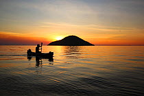 Fisherman rowing past the silhouette of Thumbe Island at sunset Lake Malawi, Cape Maclear, Malawi . June 2011