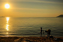 Woman and boy wash their clothes in Lake Malawi, at sunset, Cape Maclear, Malawi. June 2011