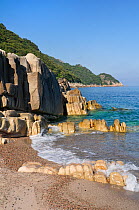 Granitic rock outcrop washed by waves, with Mediterranean forest and maquis scrub growing on the headland beyond, within a UNESCO World Natural Heritage Site and Corsica's National Park (Parc Naturel...