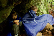 Children Russell and Jessica Laman taking shelter under a rock overhang during a tropical downpour, Gunung Palung National Park, Borneo. August 2010 Model released.