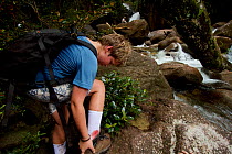 Russell Laman removing his boot to check the leach bite which is bleeding, Gunung Palung National Park, Borneo. August 2010 Model released.