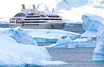 Le Lyrial expedition cruise ship sailing past icebergs, Cuverville Island, Antarctic Peninsula, Antarctica. December 2015.