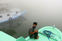 Man wearing an anti-pollution mask on a boat on the River Kumai, Tanjung Puting National Park, Central Kalimantan, Borneo, Indonesia, October 2015. In the time of illegal fires, the air becomes unbrea...