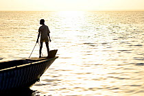 Person silhouetted on bow of boat at sunset, fishing village of Cacheu, Guinea Bissau, February 2015.