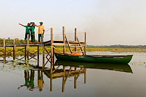 Park rangers pointing from jetty with canoe moored below, Lagoons of Cufada ( Lagoas de Cufada)  Natural Park, Guinea Bissau. February 2015