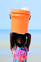 Girls standing on beach with bucket on head, on way to collect water, Orango Island, Bijagos UNESCO Biosphere Reserve, Guinea Bissau, February 2015.