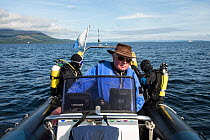 Three people in dive boat, with divers getting ready to go in water, Lamlash Bay, Isle of Arran, South Arran Marine Protected Area, Scotland, UK, August 2016.