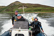 Three people including driver and two divers in dive boat with Holy Island in the background, Lamlash Bay, Isle of Arran, South Arran Marine Protected Area, Scotland, UK, August 2016.