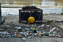 Plastic bottles washed up on a slipway of the River Thames with caged bags of rubbish and buoy behind, London Borough of Hammersmith and Fulham, England, UK, September 2015.
