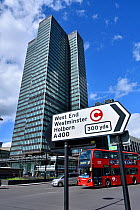 Traffic direction sign with congestion charge symbol, bus and Euston Tower in background, Euston Road, Central London, UK, March 2016.