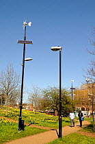 Wind and solar powered lamppost or lamp post alongside conventional lamppost with people passing, Mile End Park, London Borough of Tower Hamlets, England, UK, March 2014.