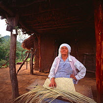 Woman weaving sleeping mat outside her home, Campo Village, aqua Caliente, Sierra Alamos, Mexico 1992