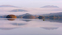 View over Derwentwater, towards Friars Crag in autumn colour and morning mist with lone rower. Near Keswick, The Lake District, Cumbria, UK. November 2016.