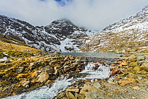 Lake Glaslyn showing the outflow the source of the Afon (River) Glaslyn with the summit of Mount Snowdon covered in cloud in the background, Snowdonia National Park, North Wales, UK, March.