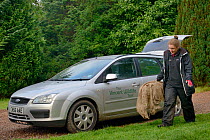 Dr. Jenny Macpherson carrying a live trap containing a Pine Marten (Martes martes) caught in Scottish woodland to a mobile vet clinic in a caravan for a radiocollar to be fitted, for a reintroduction...
