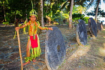 Young boy in a traditional outfit  in front of a row of stone money.  Yap, Micronesia. September 2013.