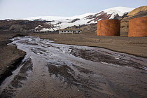 Meltwater stream with remains of fuel tanks from the whaling era 1911- 1931 and decaying building occupied by British Antarctic Survey scientists from the 1940s to 1970, Whaler's Bay, Deception Island...