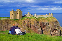 Tourists looking at Dunnottar Castle, ruined medieval fortress near Stonehaven on cliff along the North Sea coast, Aberdeenshire, Scotland, UK, May 2017