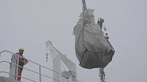 Crane lifting a bag filled with collected marine plastic for recycling onto a boat, Svalbard, Norway, August 2017.