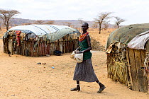Samburu woman next to improvised  huts, in dry landscape near Samburu National Reserve, Kenya, September 2017.