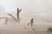 Maasai children running in a whirlwind of dust and sand. Amboseli National Park, Kenya. August 2017.