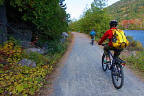 Cycling on a carriage road along a lake in Acadia National Park, Maine, USA. October 2013. Model released.