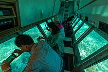 Tourists in a glass bottom boat looking at corals around the shallow reefs of Green Island, Green Island, Great Barrier Reef, Queensland, Australia October 2016.