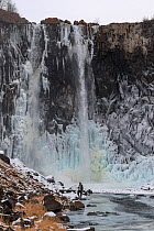 Photographer standing at the base of waterfall which is starting to freeze over. Putoransky State Nature Reserve, Putorana Plateau, Siberia, Russia