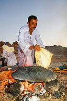 Bedouin man cooking bread on an open fire, Sinai Desert, Dahab,  Egypt. October 2008.