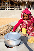Woman subsistence farmer cooking on a traditional clay oven, using rice stalks as biofuel in the Sunderbans, Ganges Delta, India. December 2013.