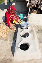Woman subsistence farmer cooking on a traditional clay oven, using rice stalks as biofuel in the Sunderbans, Ganges Delta, India. 2013.