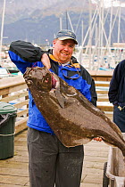 Man with a Pacific halibut (Hippoglossus stenolepis) caught during sport fishing, Seward, Alaska, USA, September 2004.