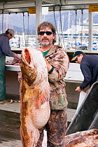 Man with a Ling Cod (Ophiodon elongatus) caught during sport fishing, Seward, Alaska, USA, September.