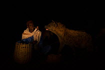 Man feeding Spotted hyenas (Crocuta crocuta) at night, Harar, Ethiopia, December 2017.