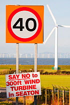 Protest sign about a new wind turbine in Seaton near Workington, Cumbria, UK, with onshore wind turbines and the offshore Robin Rigg wind farm visible. January 2012