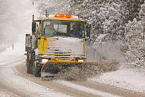 A snow plough driving in heavy snow, clearing the road  in Ambleside, England, UK. March 2006
