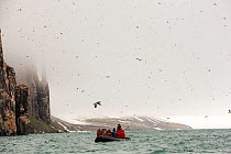 Passengers on Zodiaks off the Russian research vessel, AkademiK Sergey Vavilov an ice strengthened ship on an expedition cruise to Northern Svalbard in front of the Aalkefjellet, sea bird nesting clif...