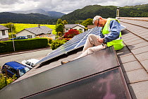 Workman fitting solar thermal panels for heating water, to a house roof, Ambleside, Cumbria, UK,. June 2012